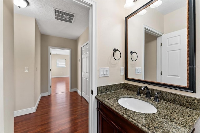 bathroom featuring visible vents, vanity, a textured ceiling, wood finished floors, and baseboards