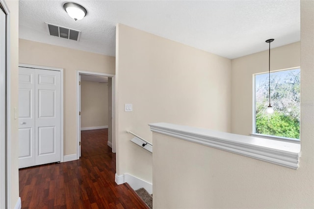 hallway with a textured ceiling, wood finished floors, visible vents, and baseboards