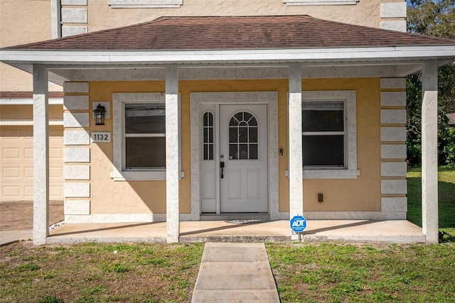 property entrance with stucco siding, covered porch, and roof with shingles