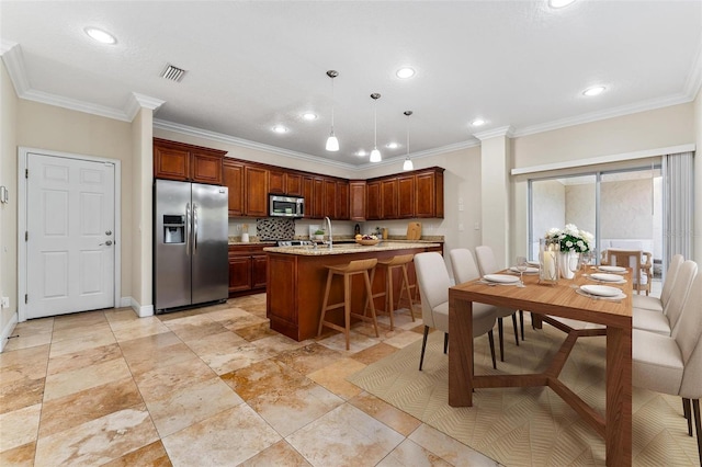 kitchen featuring visible vents, a kitchen breakfast bar, appliances with stainless steel finishes, ornamental molding, and pendant lighting