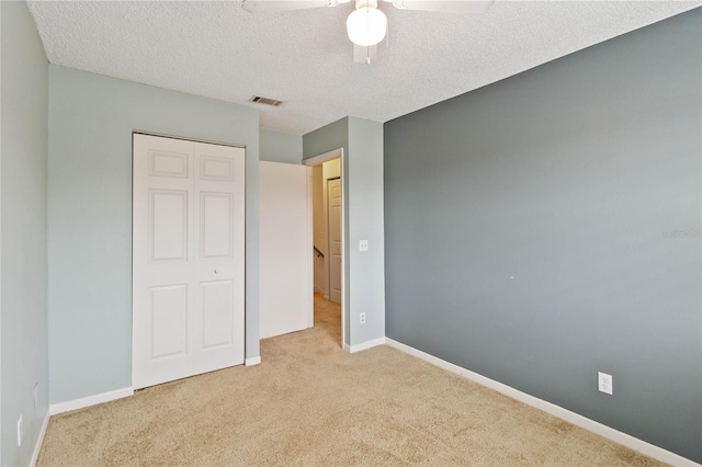 unfurnished bedroom featuring a closet, light colored carpet, visible vents, a textured ceiling, and baseboards