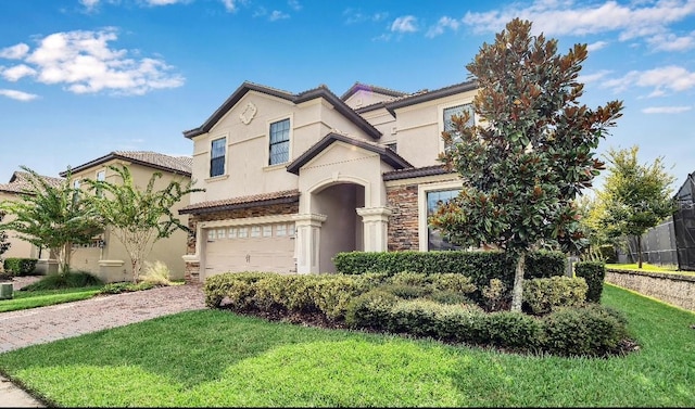 mediterranean / spanish-style home featuring stone siding, an attached garage, decorative driveway, a front yard, and stucco siding