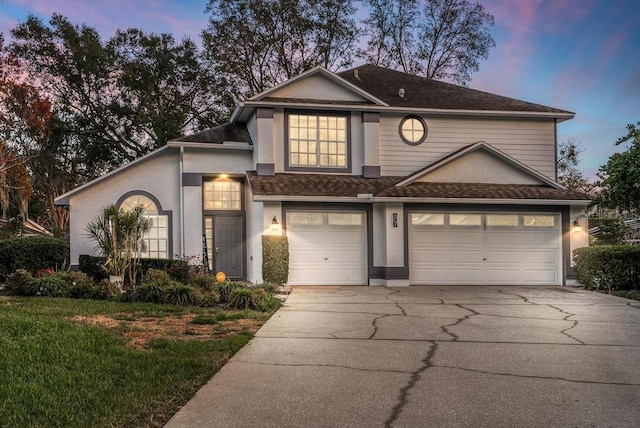 traditional-style home with driveway, a shingled roof, and stucco siding