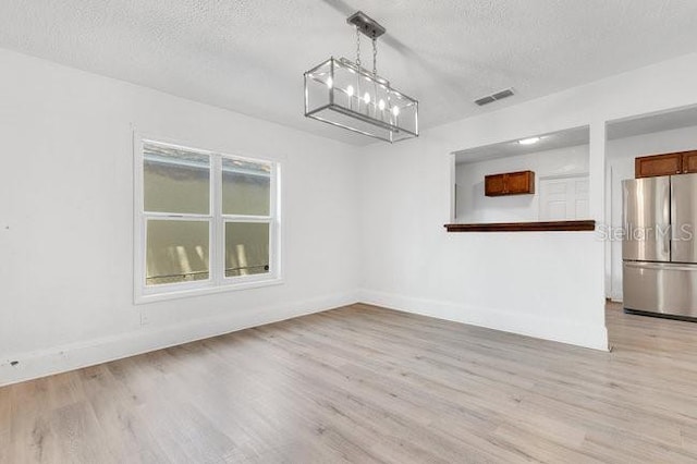 unfurnished room with baseboards, a textured ceiling, and light wood finished floors