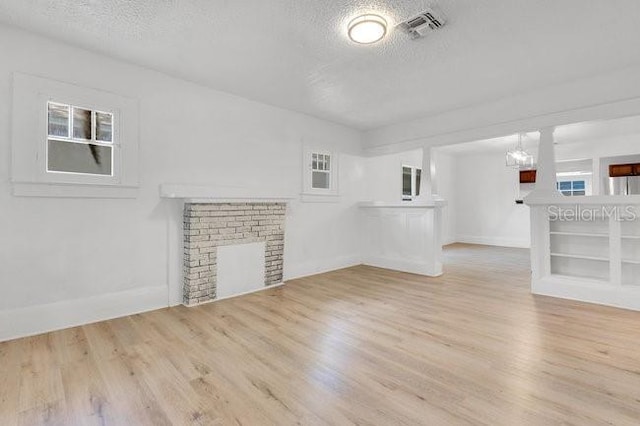 unfurnished living room with a textured ceiling, wood finished floors, plenty of natural light, and a chandelier