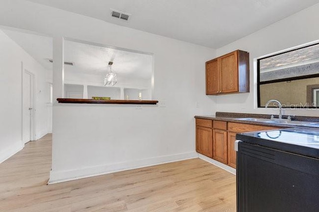 kitchen featuring brown cabinetry, light wood-style flooring, baseboards, a sink, and dark countertops