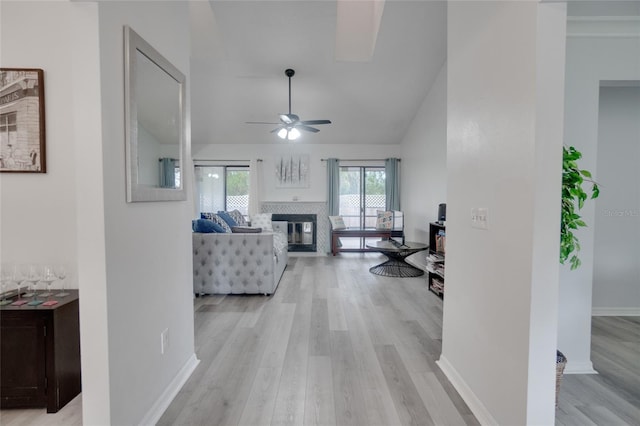 living area with a glass covered fireplace, light wood finished floors, ceiling fan, and baseboards