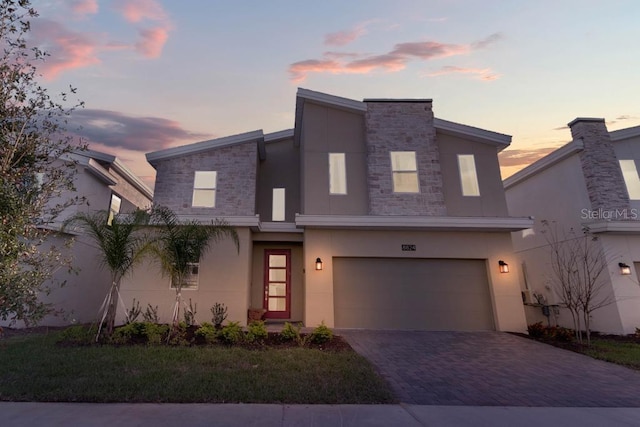 modern home featuring a garage, stone siding, decorative driveway, and stucco siding