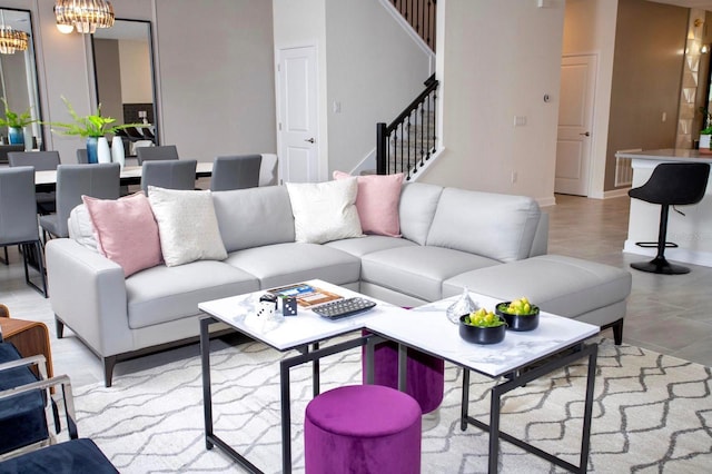 living room featuring an inviting chandelier, baseboards, and stairway