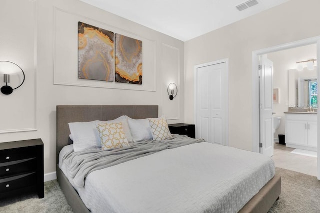 bedroom with ensuite bath, visible vents, a closet, and light colored carpet