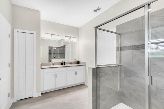 bathroom featuring a sink, visible vents, a closet, double vanity, and a stall shower