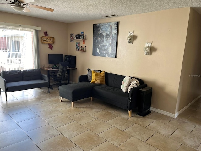 living room featuring a textured ceiling, light tile patterned floors, a ceiling fan, and baseboards