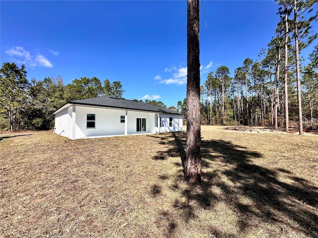 back of property featuring a lawn and stucco siding