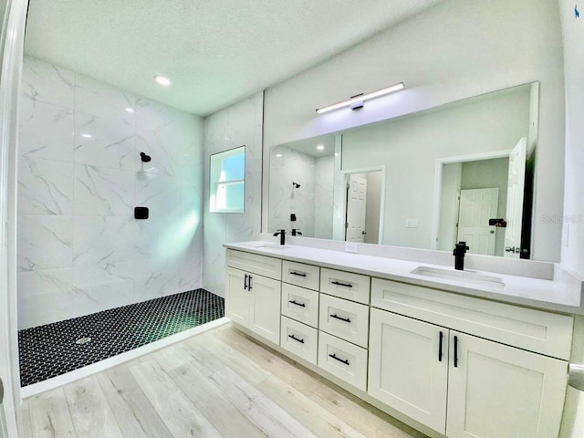 full bathroom featuring double vanity, a marble finish shower, a sink, and wood finished floors