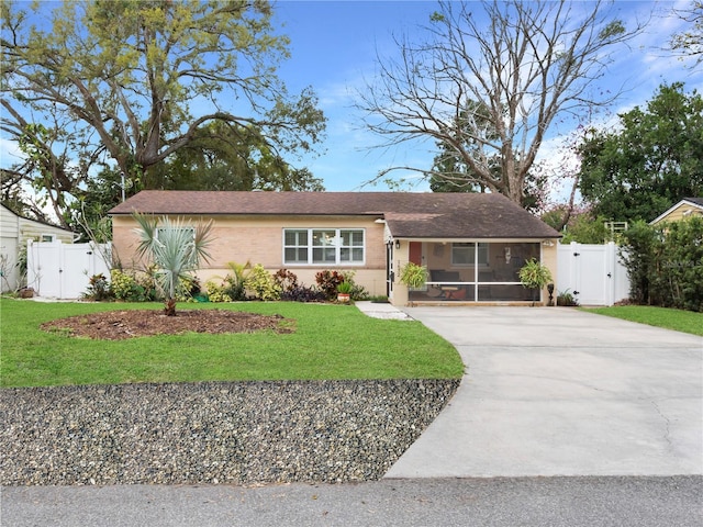 ranch-style house featuring concrete driveway, a sunroom, a gate, fence, and a front lawn