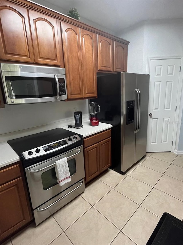 kitchen featuring brown cabinets, light tile patterned floors, stainless steel appliances, and light countertops