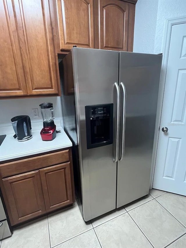 kitchen with light tile patterned floors, light countertops, brown cabinetry, and stainless steel fridge with ice dispenser