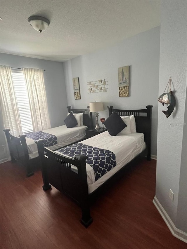 bedroom featuring baseboards, dark wood finished floors, and a textured ceiling