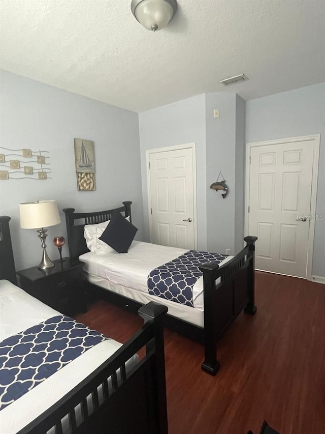 bedroom with a textured ceiling, visible vents, and dark wood-type flooring