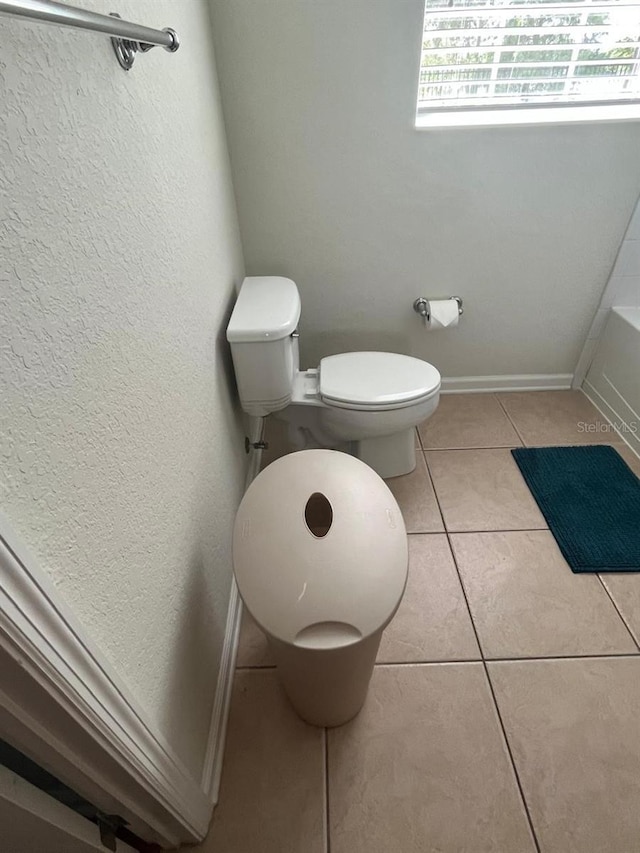 bathroom with a bath, toilet, baseboards, and tile patterned floors