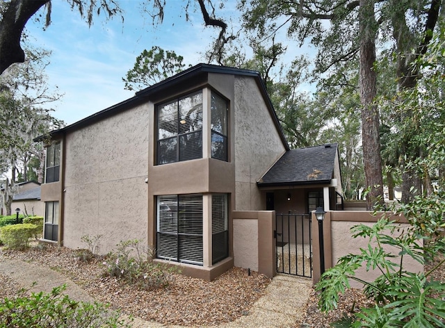 view of front of property with a shingled roof, fence, a gate, and stucco siding