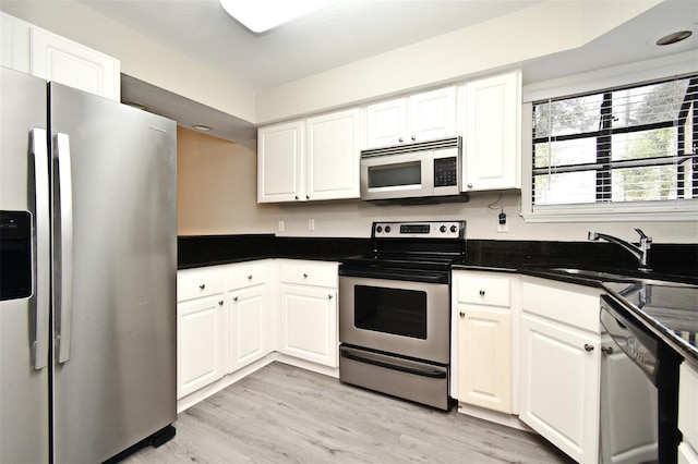 kitchen featuring stainless steel appliances, dark countertops, white cabinetry, and a sink