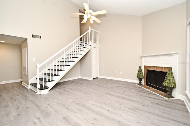 unfurnished living room featuring baseboards, visible vents, a tile fireplace, stairway, and light wood-type flooring