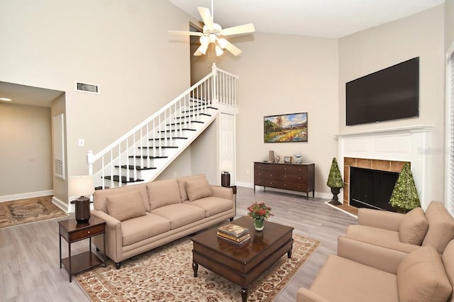 living room with a tile fireplace, visible vents, baseboards, light wood-style floors, and stairway