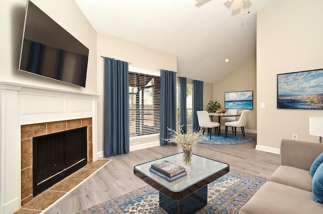 living room featuring baseboards, a ceiling fan, vaulted ceiling, light wood-type flooring, and a fireplace