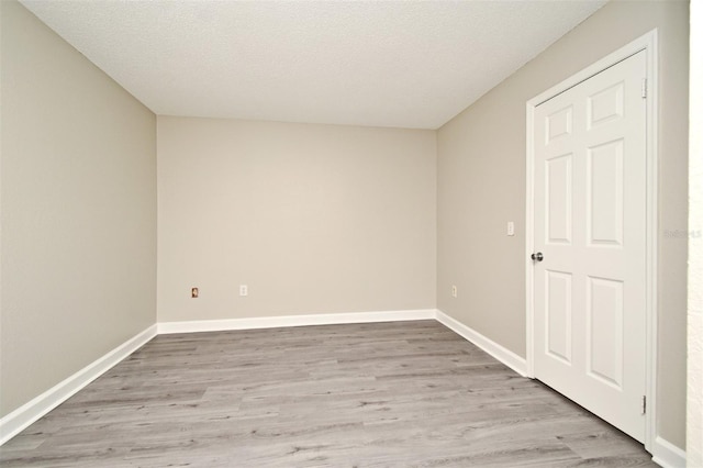 empty room featuring baseboards, a textured ceiling, and light wood-style floors