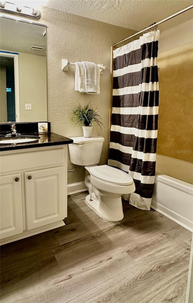 full bath featuring a textured wall, a textured ceiling, toilet, and wood finished floors