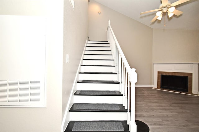 stairway with a tiled fireplace, wood finished floors, a ceiling fan, and baseboards