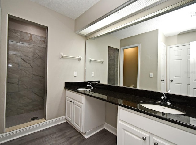 bathroom with double vanity, tiled shower, a sink, and wood finished floors