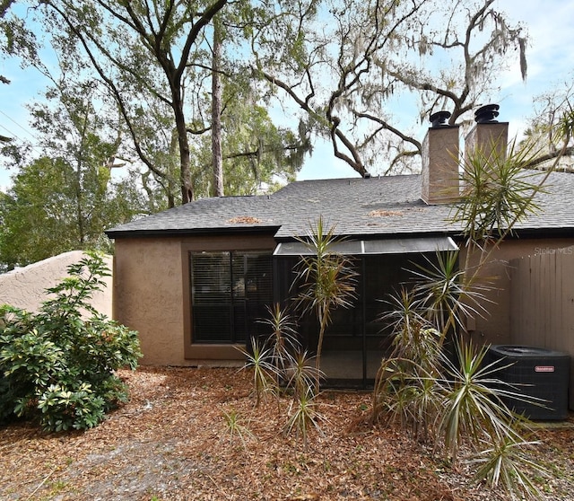 back of house featuring roof with shingles, a chimney, central AC, and stucco siding