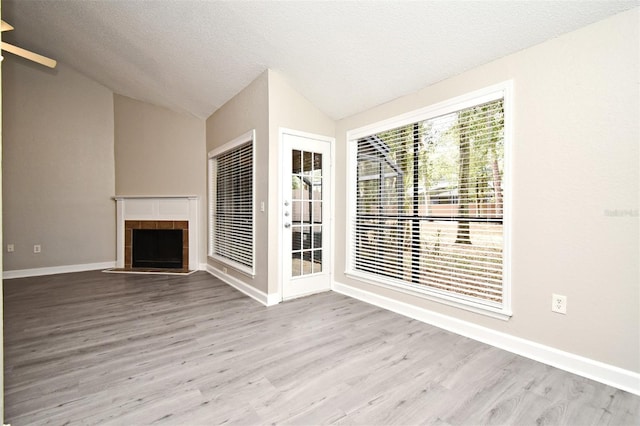 unfurnished living room with a textured ceiling, a tile fireplace, baseboards, vaulted ceiling, and light wood-style floors