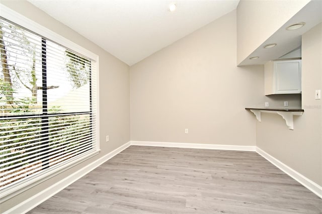 unfurnished room featuring light wood-type flooring, vaulted ceiling, and baseboards