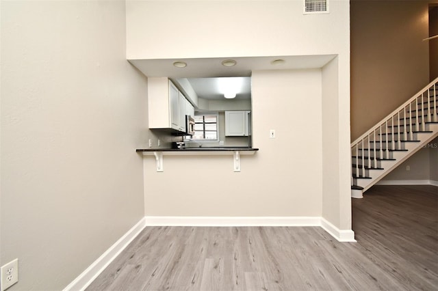 kitchen with dark countertops, visible vents, white cabinetry, light wood-type flooring, and baseboards