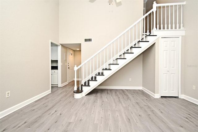 stairway with a towering ceiling, baseboards, visible vents, and wood finished floors