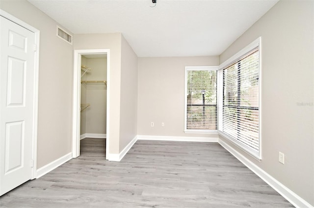 unfurnished bedroom with visible vents, baseboards, a closet, light wood-type flooring, and a walk in closet