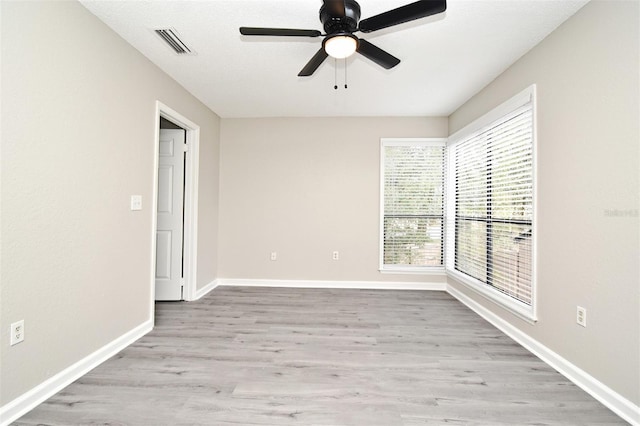 spare room featuring baseboards, a ceiling fan, visible vents, and light wood-style floors