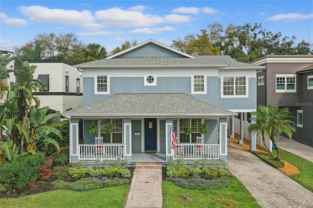 view of front facade featuring decorative driveway, covered porch, a shingled roof, and stucco siding