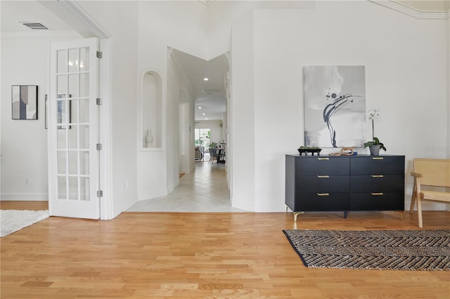 corridor with light wood-type flooring, visible vents, crown molding, and a towering ceiling