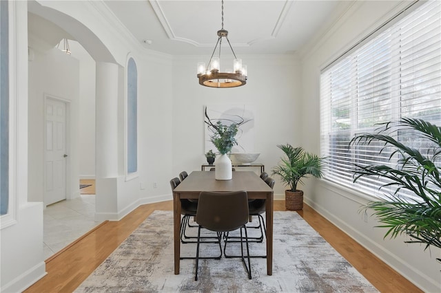 dining area with baseboards, light wood-style flooring, arched walkways, and crown molding