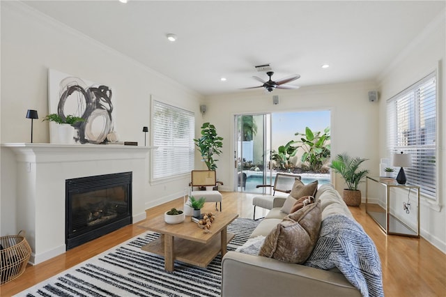 living room with light wood finished floors, visible vents, crown molding, and a glass covered fireplace