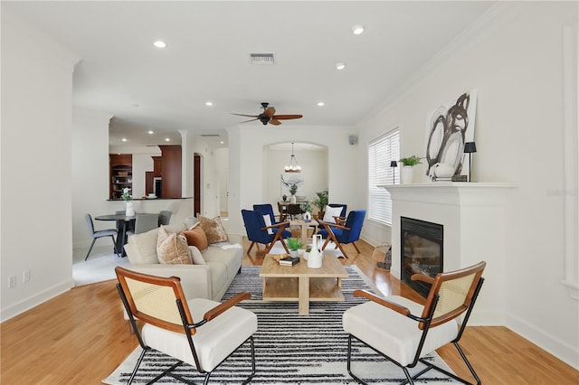 living area featuring arched walkways, visible vents, light wood finished floors, a glass covered fireplace, and crown molding