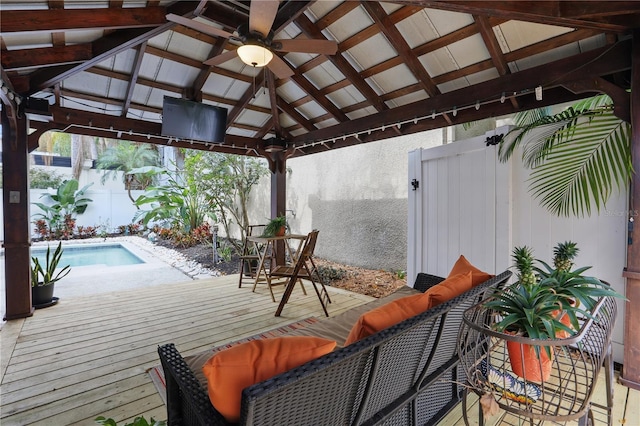 wooden terrace featuring outdoor lounge area, a gazebo, a ceiling fan, fence, and an outdoor pool