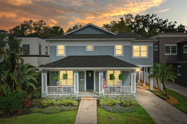 view of front of property featuring a porch, decorative driveway, roof with shingles, and stucco siding