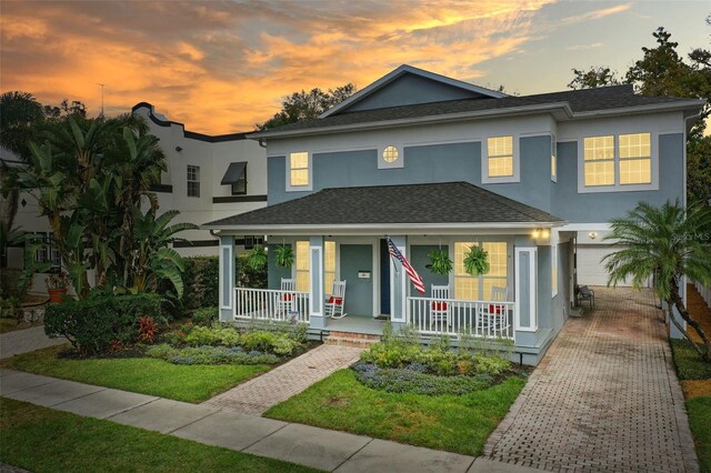 view of front of property featuring roof with shingles, a porch, decorative driveway, and stucco siding