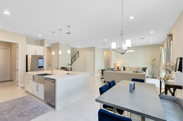 kitchen featuring an island with sink, hanging light fixtures, stainless steel appliances, light countertops, and a sink