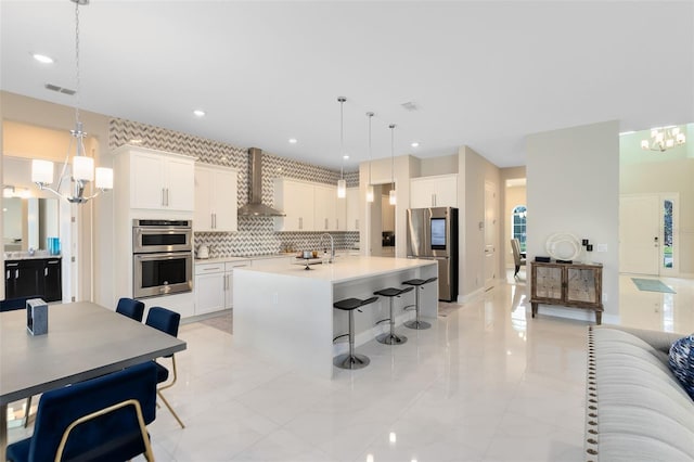 kitchen featuring pendant lighting, stainless steel appliances, light countertops, white cabinets, and wall chimney exhaust hood